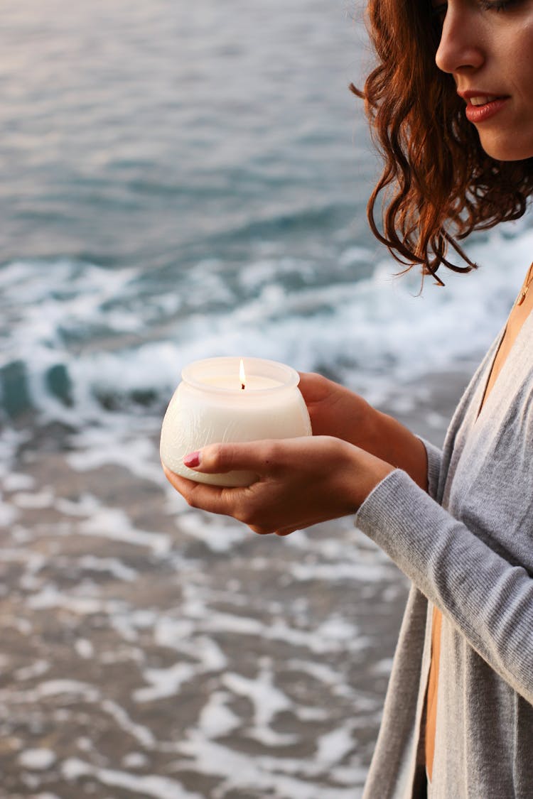 Woman Holding Lit Candle With Sea In Background