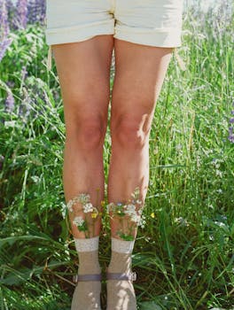 A close-up view of a woman's legs in a meadow adorned with wildflowers on a sunny day.