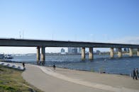 一座大桥横跨河流，人们在桥下散步和骑自行车，构成了一幅城市景观