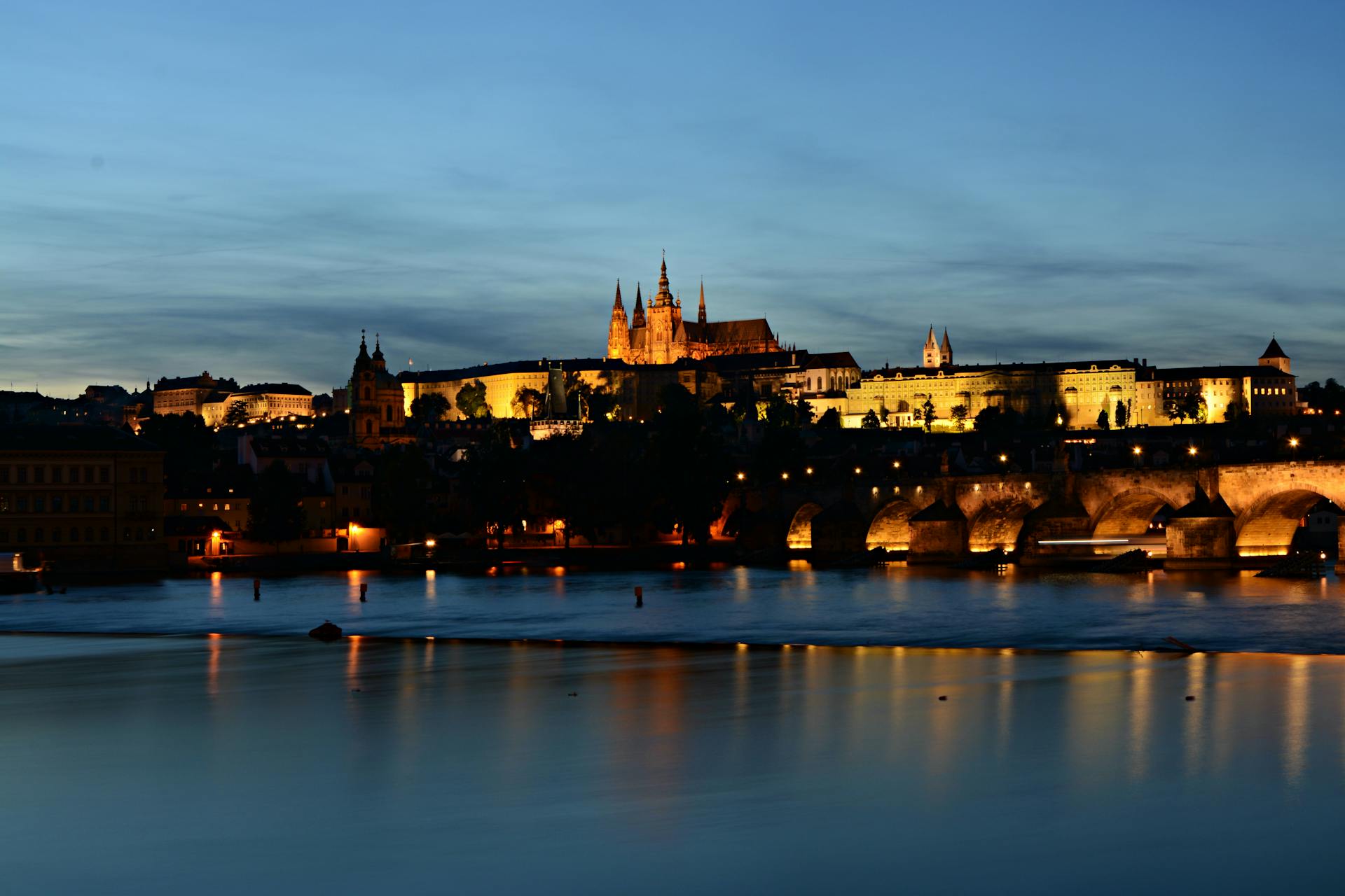 Beautiful view of Prague Castle and Charles Bridge reflecting on Vltava River at dusk.