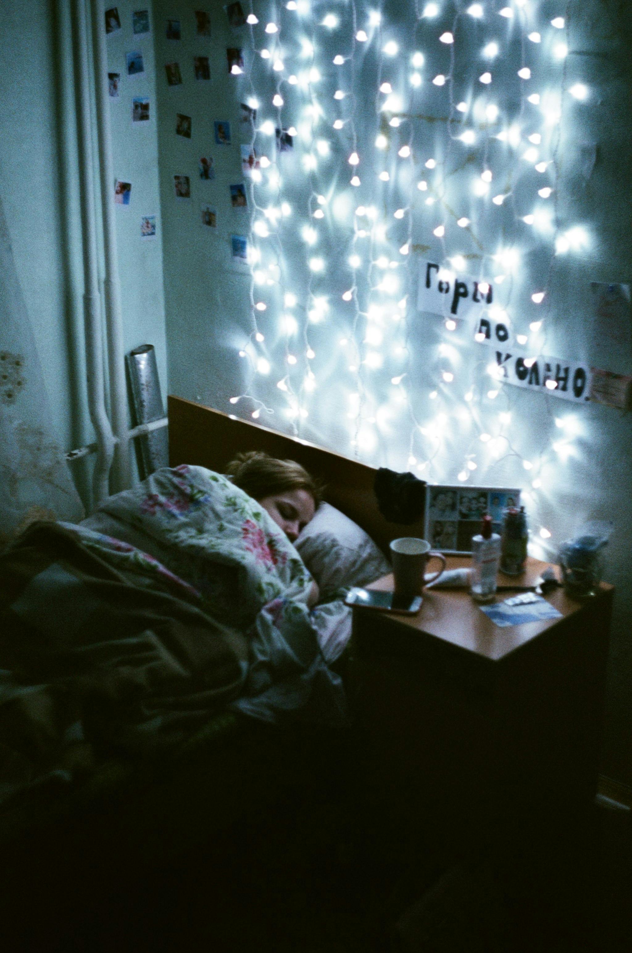 A woman sleeping in a cozy bedroom illuminated by warm string lights, creating a serene atmosphere.