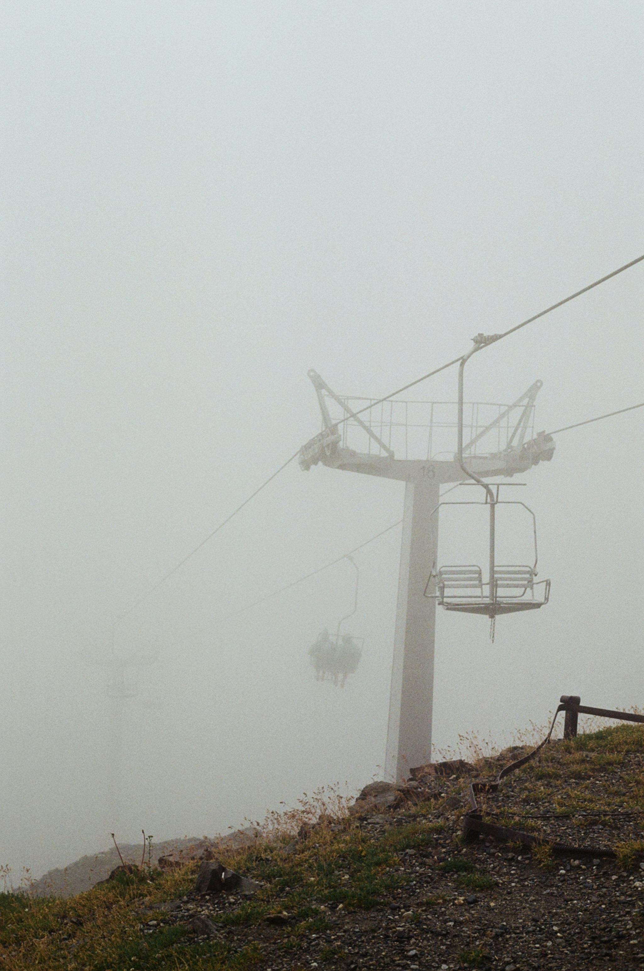 A serene view of a ski lift shrouded in dense fog on a misty mountain.