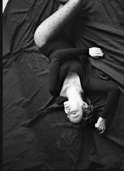 Black and white portrait of a woman lying on a bed with eyes closed in artistic pose.