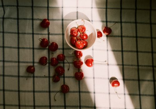 Free A bowl of fresh cherries on a patterned cloth with sunlight creating a warm, rustic look. Stock Photo
