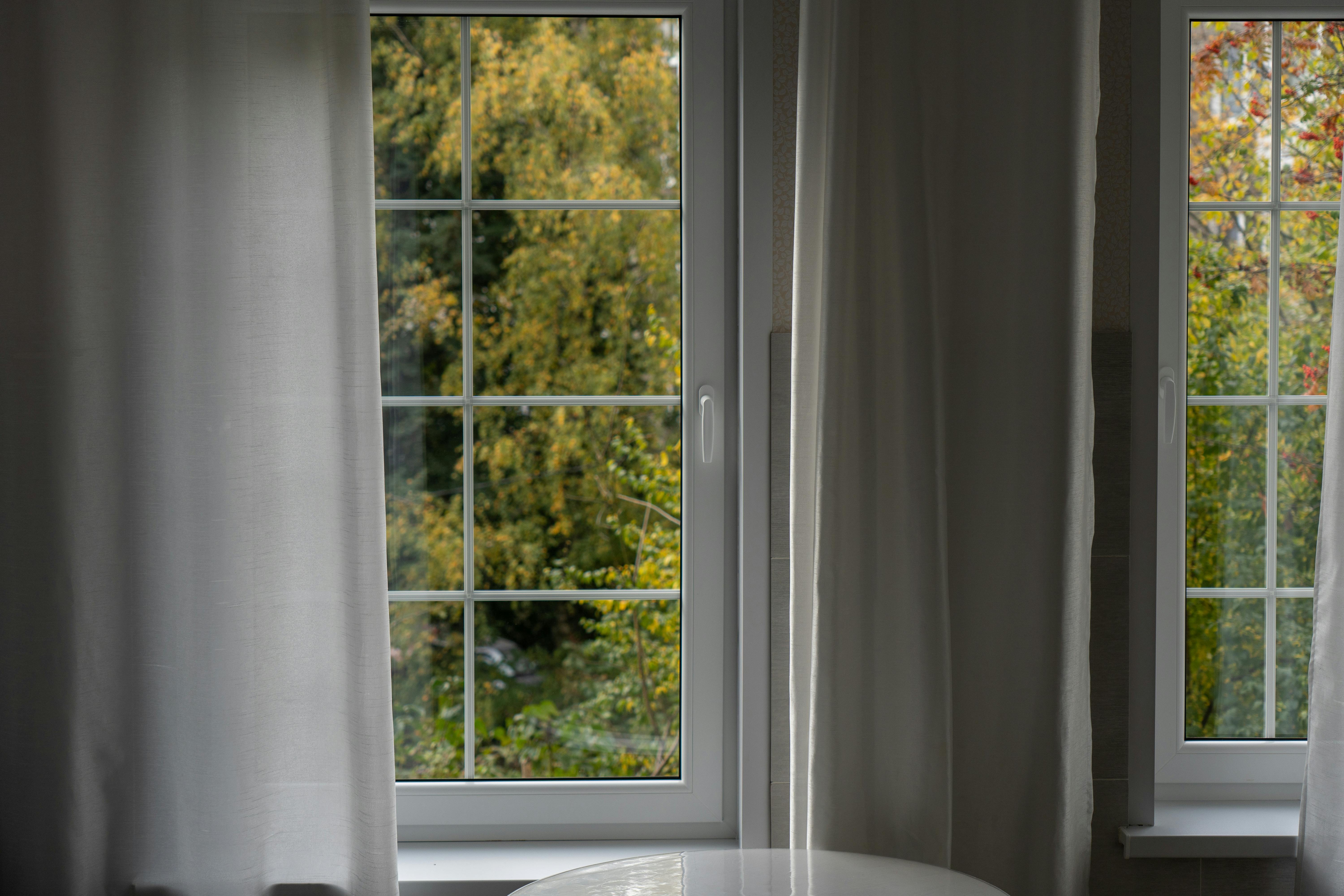 Serene interior with white curtains framing a lush green outdoor view through a window.