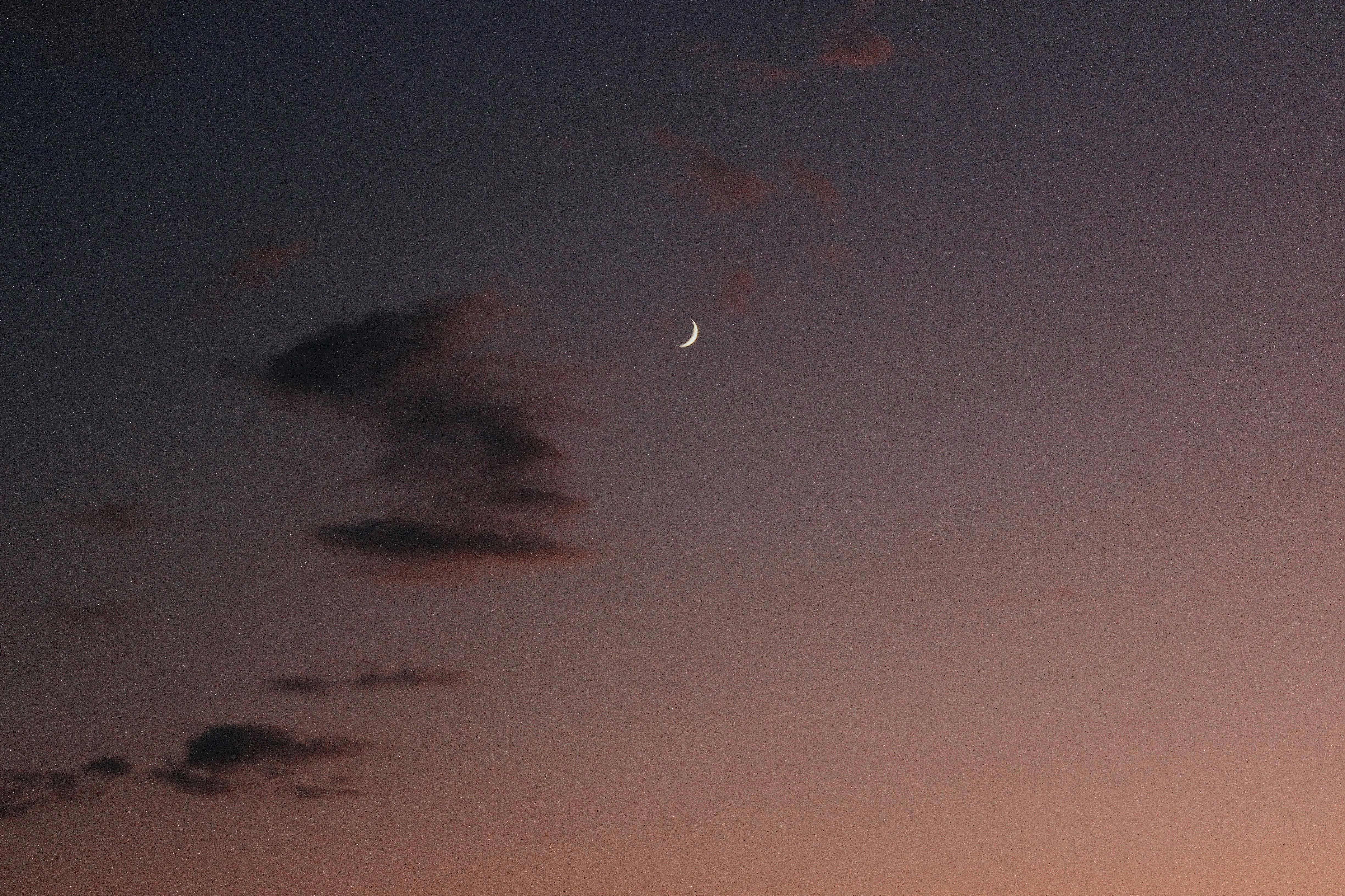 A tranquil scene of a crescent moon with scattered clouds against a purple dusk sky, perfect for dreamy backgrounds.