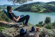 在阿尔及利亚布利达，一名男子在湖泊旁放松，湖泊四周环绕着山丘和绿地，风景优美