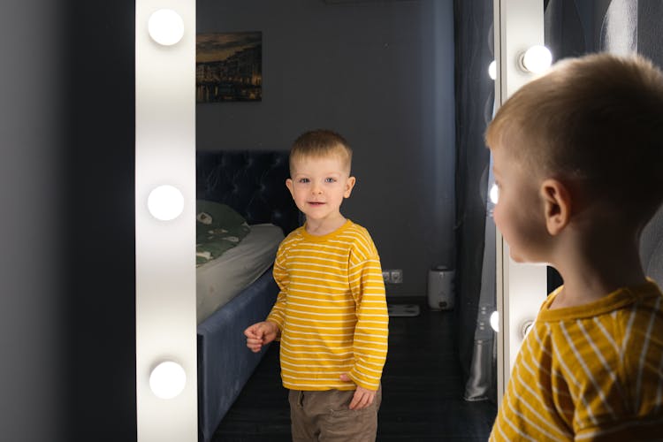 A Boy Looking At A Mirror With Light Bulbs 