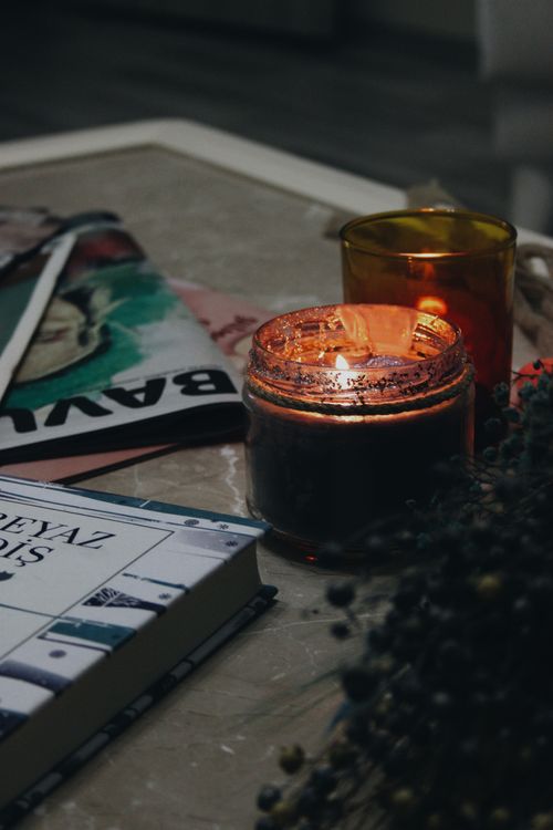 Free A warm, tranquil setting with a lit candle, books, and magazines on a table - perfect for a relaxing evening. Stock Photo