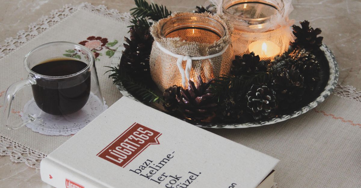 A warm, softly lit living room with a chunky knit blanket, a book on a side table, and a flickering candle on a wooden coffee table