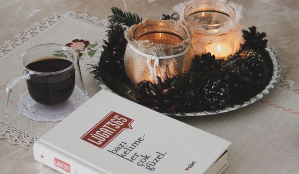 A warm and cozy setup featuring candles, a book, and a glass of coffee on a decorated table.