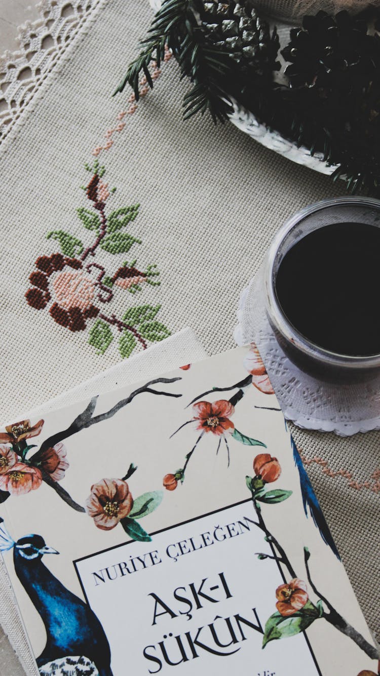 Book And Cup Of Coffee Lying On Embroidered Tablecloth