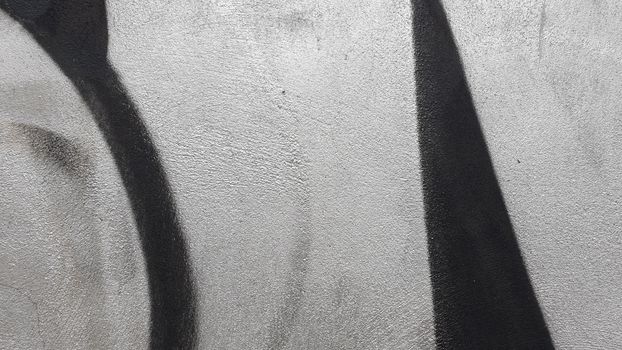 Black and white abstract graffiti on a textured concrete wall with shadows.