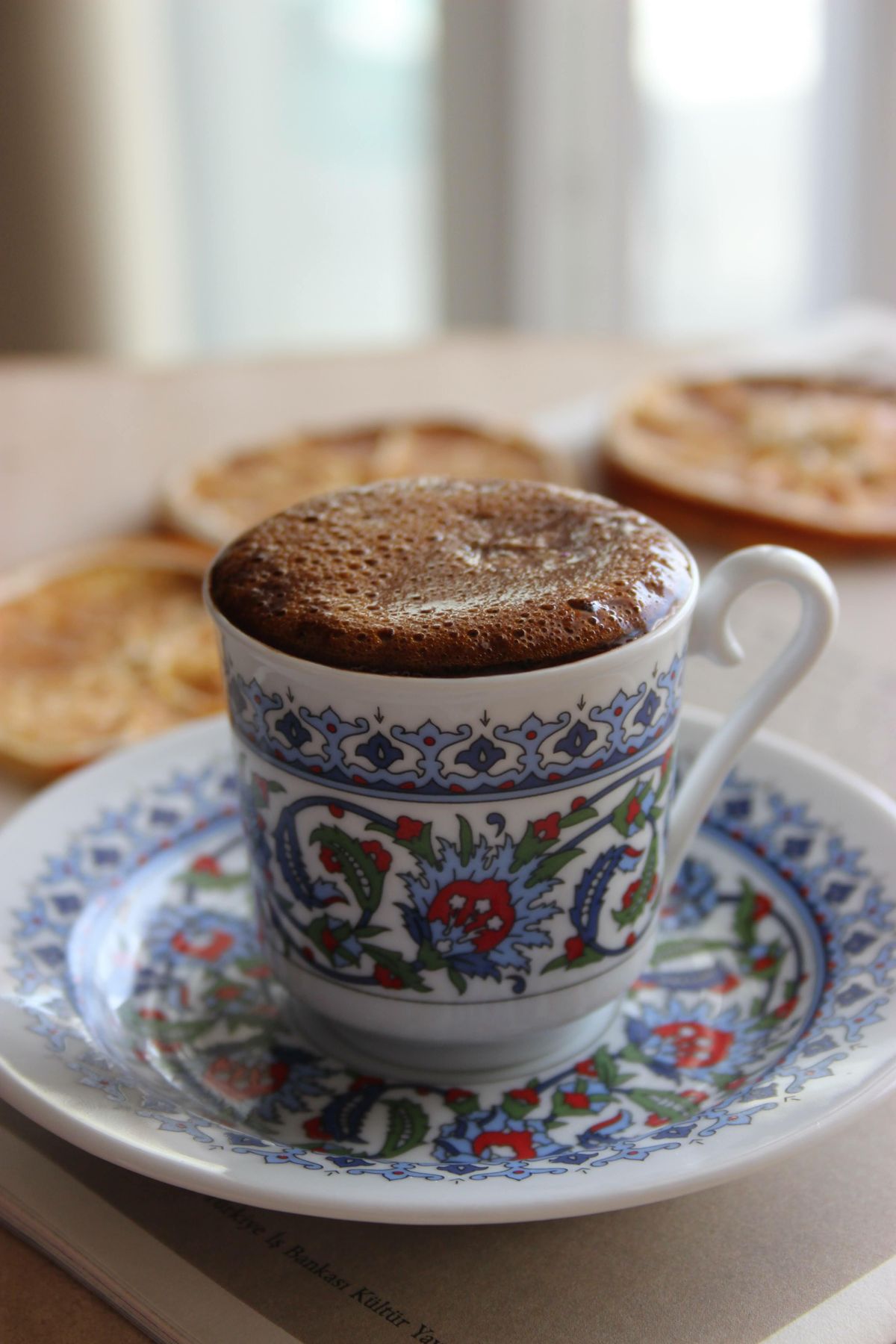 Cafea la ibric servită într-o ceașcă decorativă, cu strat gros de caimac maroniu deasupra