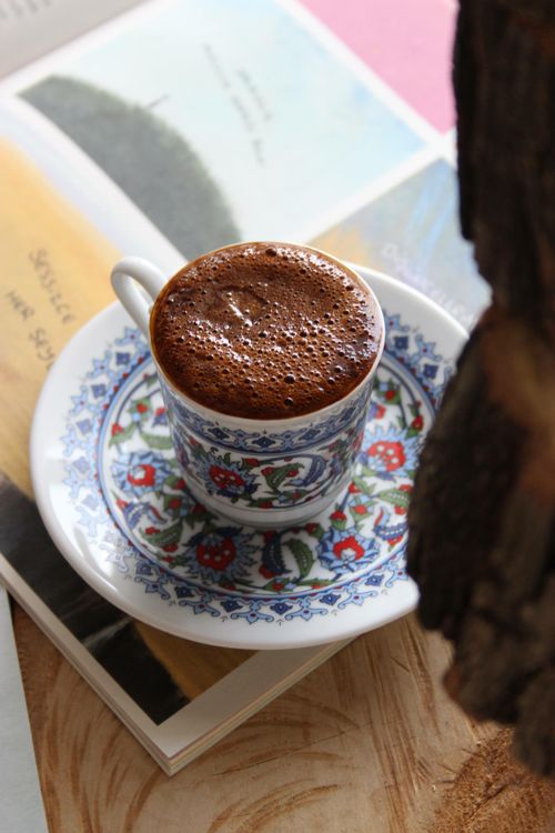 Free Artfully designed cup of hot chocolate served on a floral saucer atop an open book. Stock Photo