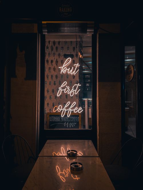 Free Dimly lit cafe with neon 'but first coffee' sign, tables, and ashtrays. Stock Photo