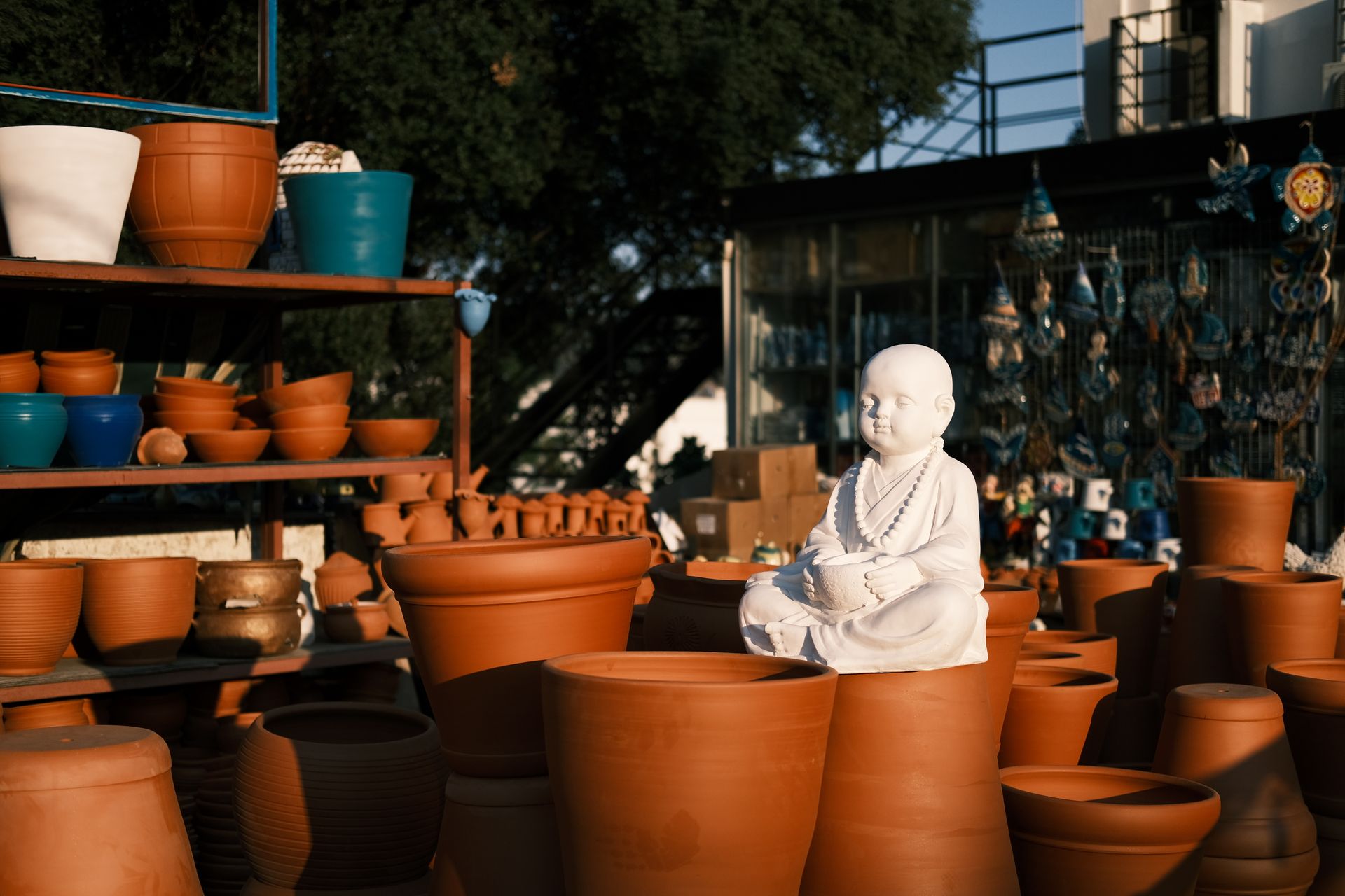 Serene Buddha sculpture surrounded by handmade terracotta pottery in an outdoor setting.