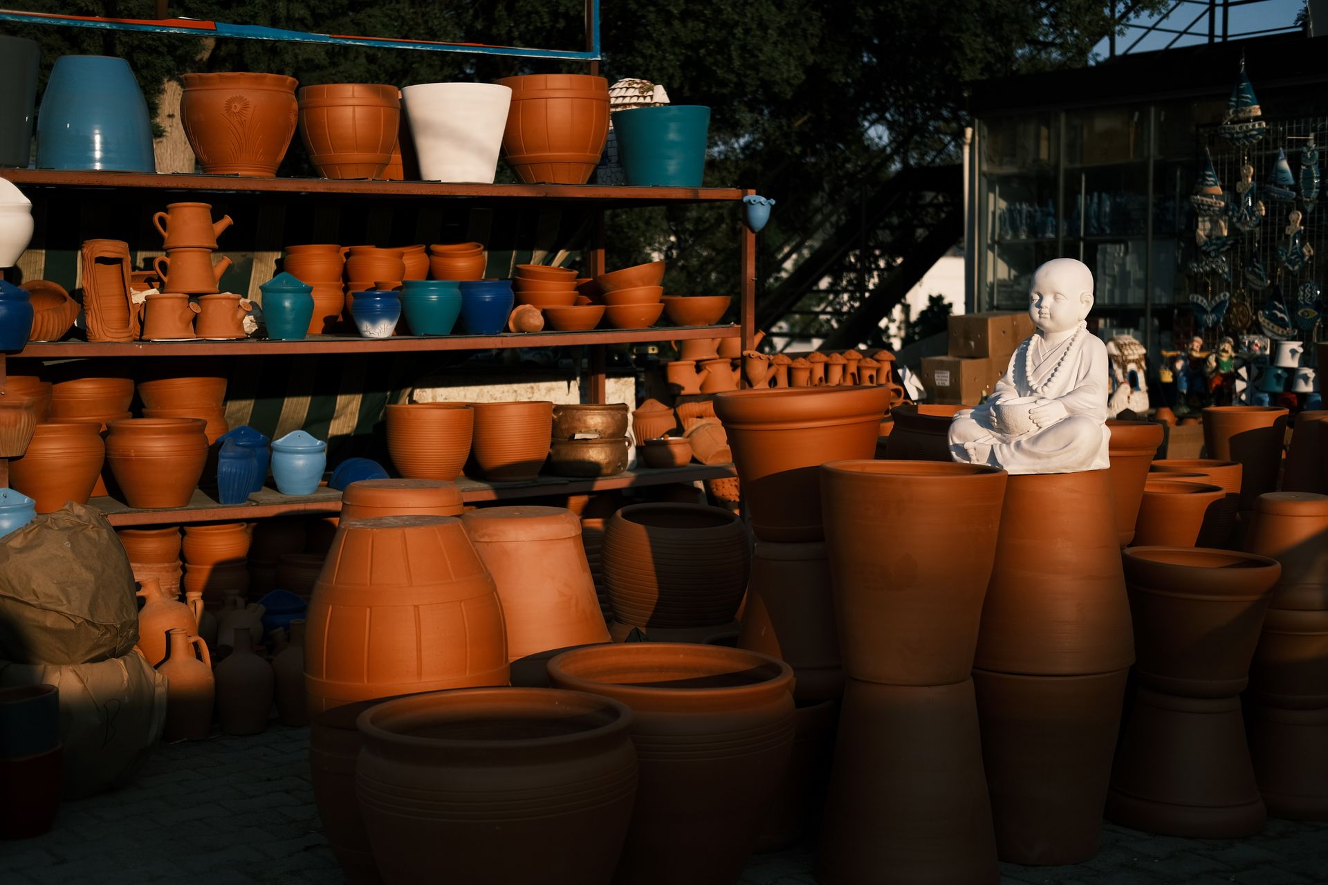A collection of clay pots and sculptures in warm lighting on wooden shelves, showcasing handmade art.