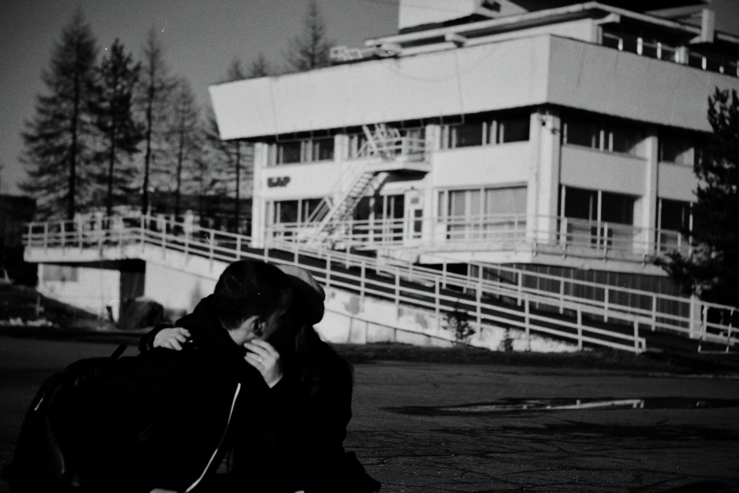 A couple embraces in front of a modern building in grayscale, capturing a heartfelt urban moment.