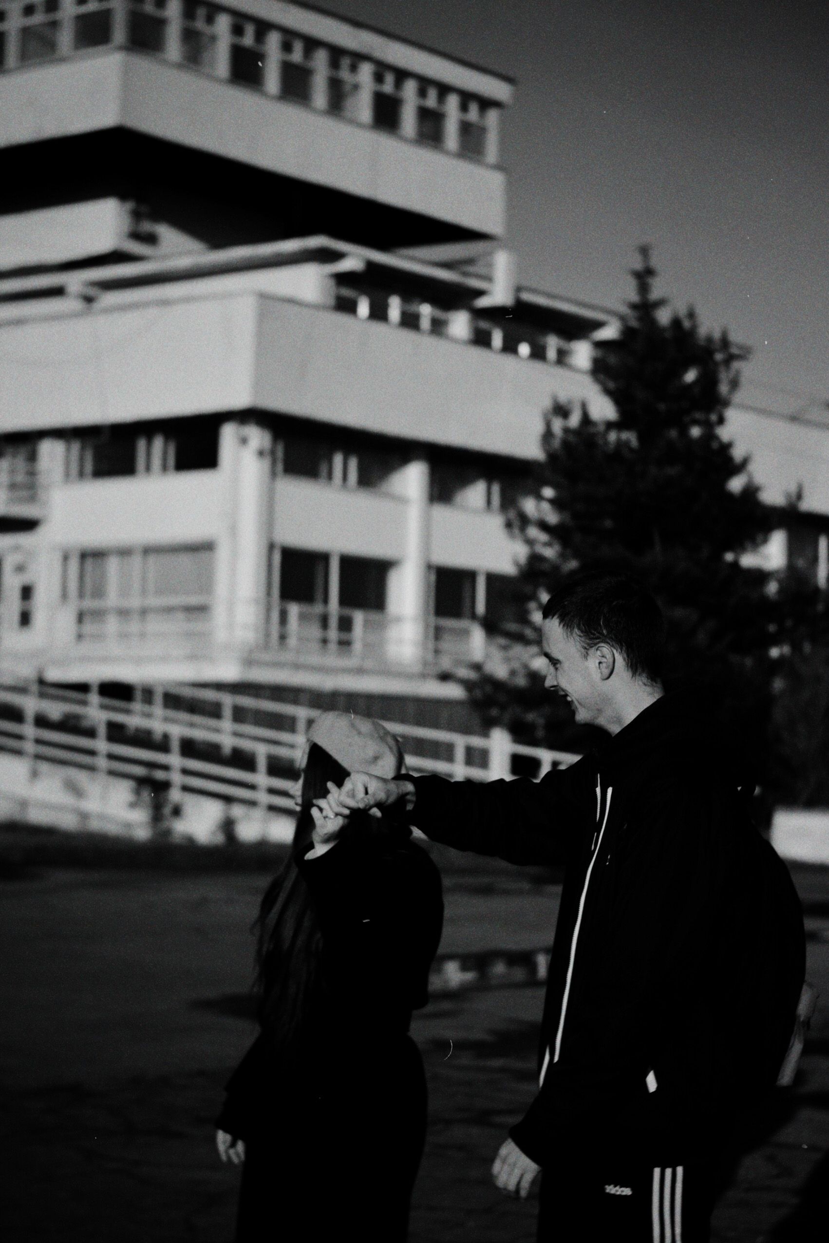A couple in black and white interacting outdoors near a modern architectural structure.