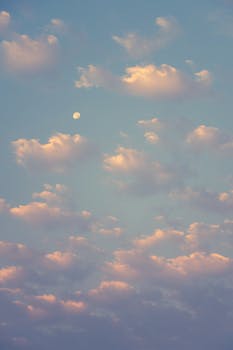 Soft clouds against a pastel sky with a visible moon in daylight.