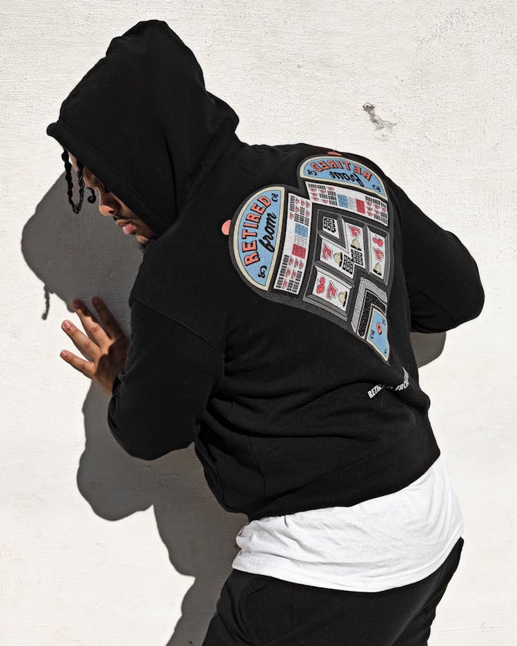 Man With Hood Obscuring His Face Touching White Wall