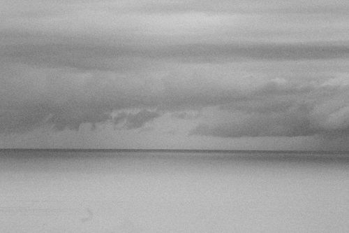 Free Grainy black and white image of a calm ocean with cloudy sky and horizon. Stock Photo