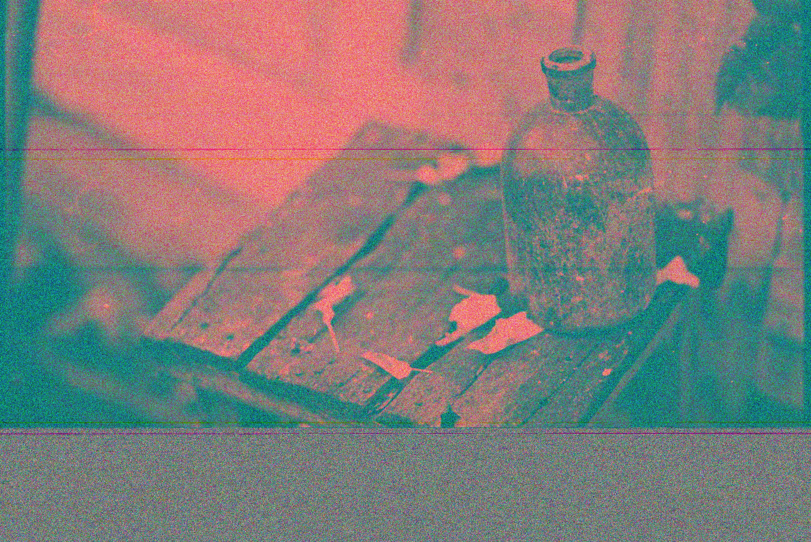 Artistic photo of a vintage glass bottle on a weathered wooden table with a textured, sooty appearance.