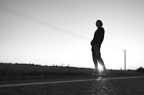 Grayscale Photo of a Man Standing on a Road Near a Field