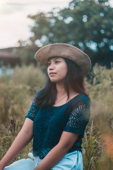 Young woman in a blue top with a straw hat sitting in a grassy field, expressing serenity.