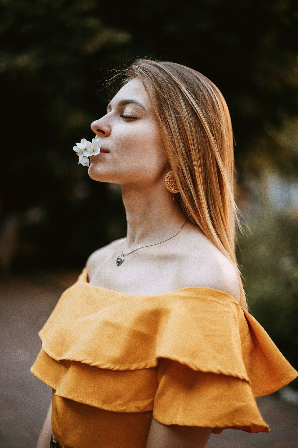 Close-up portrait of a woman in a mustard off-shoulder ruffled top holding a white flower