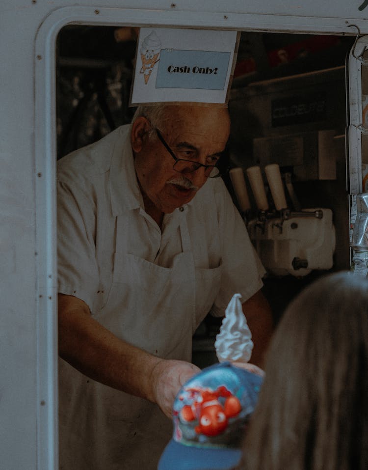 An Elderly Man Serving A Cone Of Ice Cream