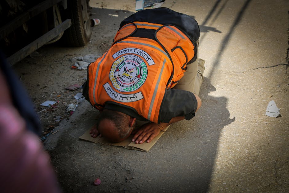 An emergency worker in an orange vest prays on a street in Gaza, depicting a moment of faith amidst turmoil.
