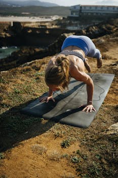 Woman performing yoga pose on mat outdoors with scenic background.