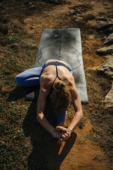 Adult woman stretching in a yoga pose on a mat outdoors, emphasizing health and fitness.