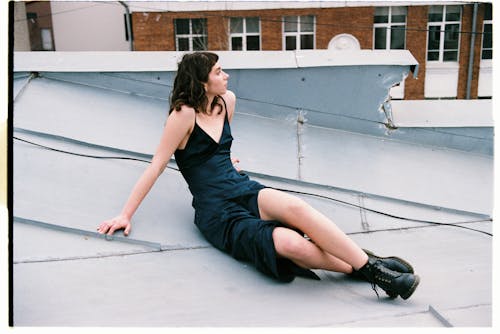 Free A Woman in Black Dress Sitting in the Roof of a House while Looking Afar Stock Photo
