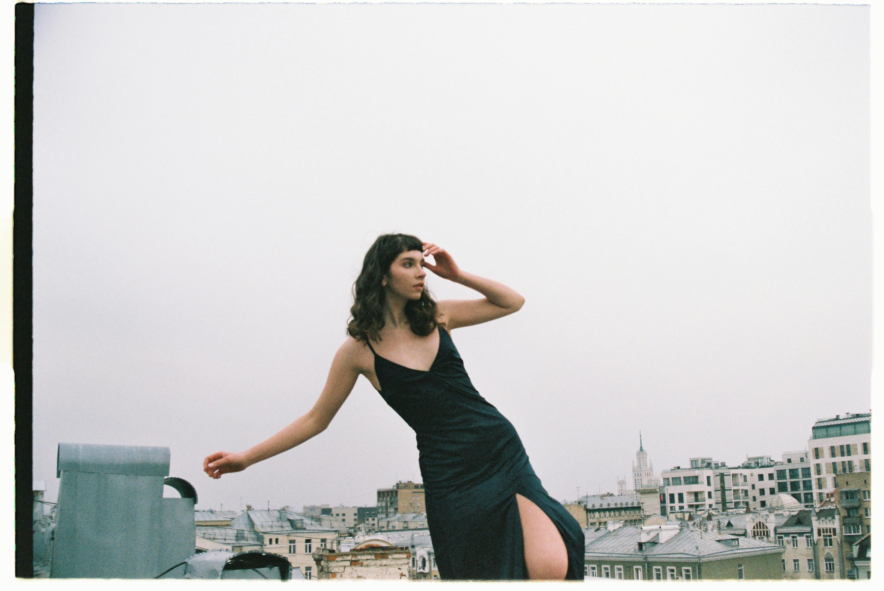 Elegant woman in black dress posing on a rooftop with Moscow skyline in the background.