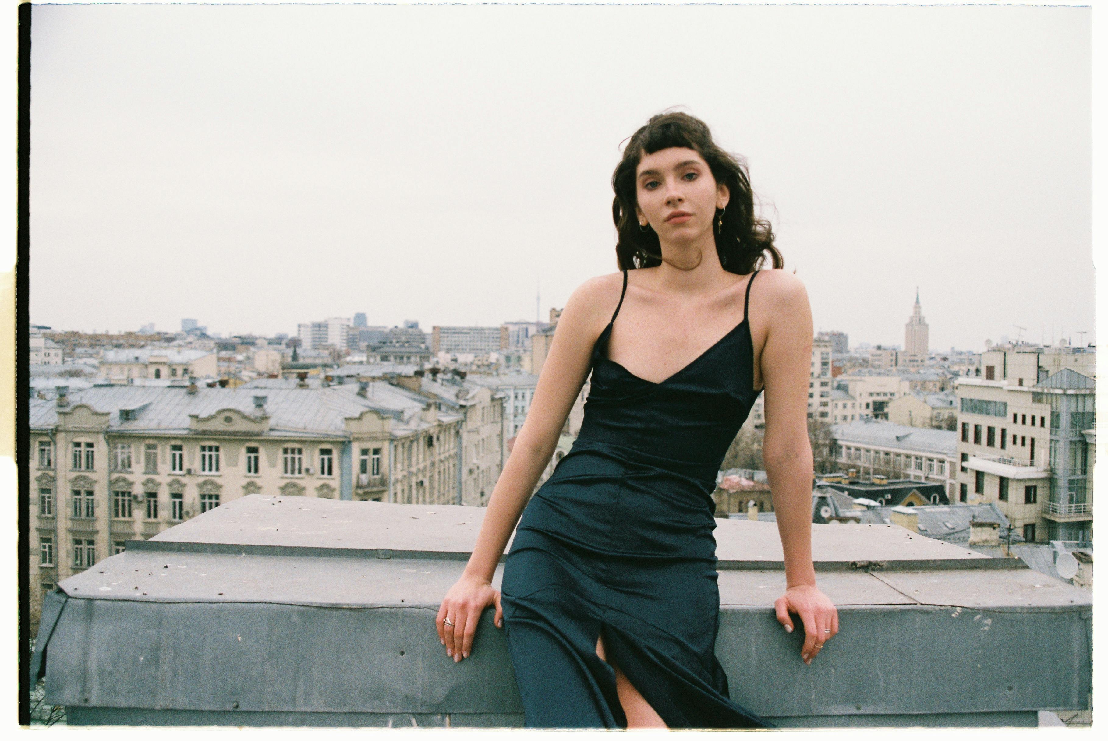 Elegant woman in black dress posing on a rooftop with a scenic Moscow skyline.