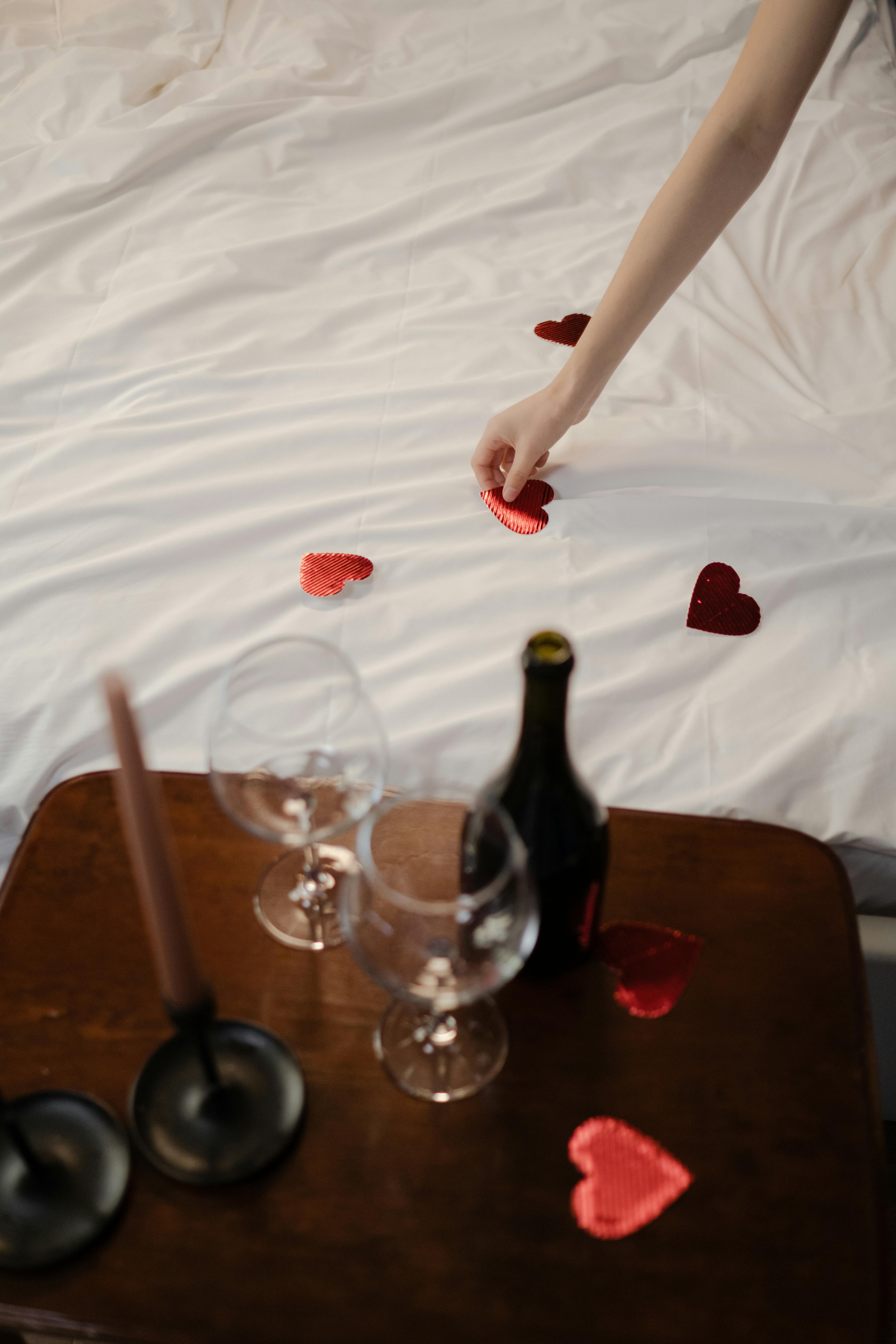 Elegant romantic setup with wine glasses and heart decorations on a cozy bed.