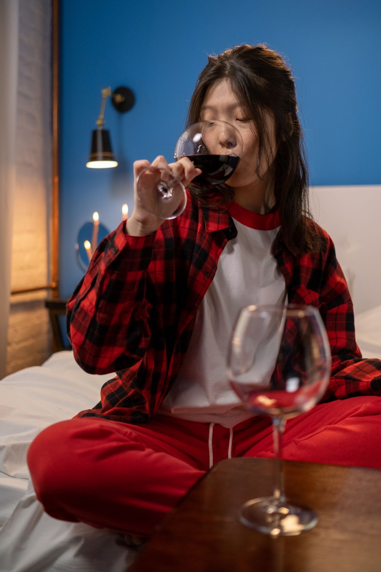 Woman in red plaid flannel pajamas drinking wine in bed