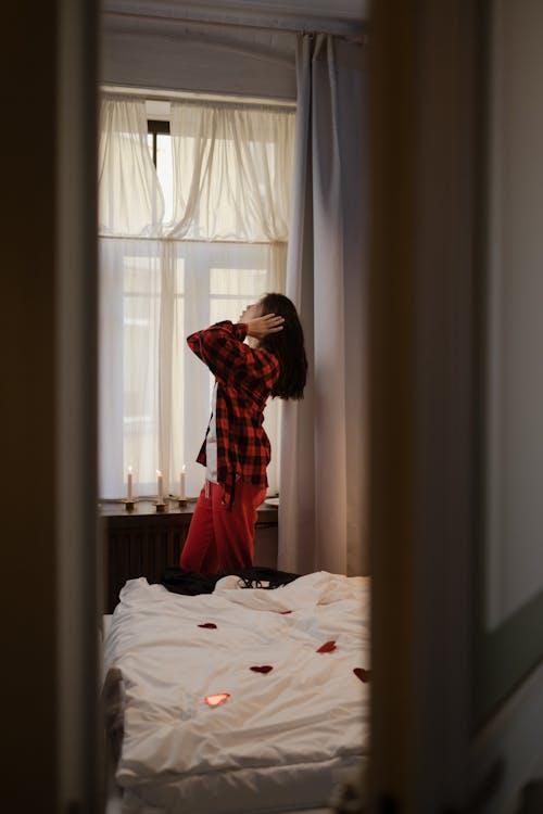 Woman in Her Pajamas Standing by Window in Bedroom