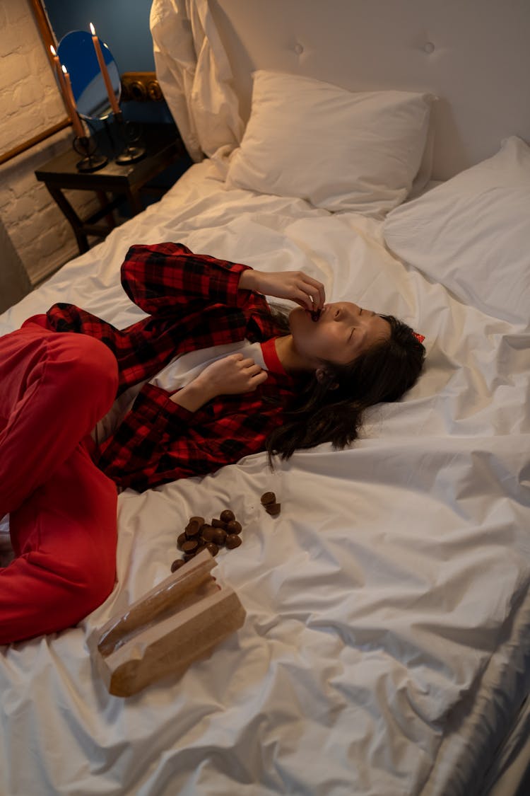 Single Woman Lying In Bed And Eating Chocolates On Valentines Day