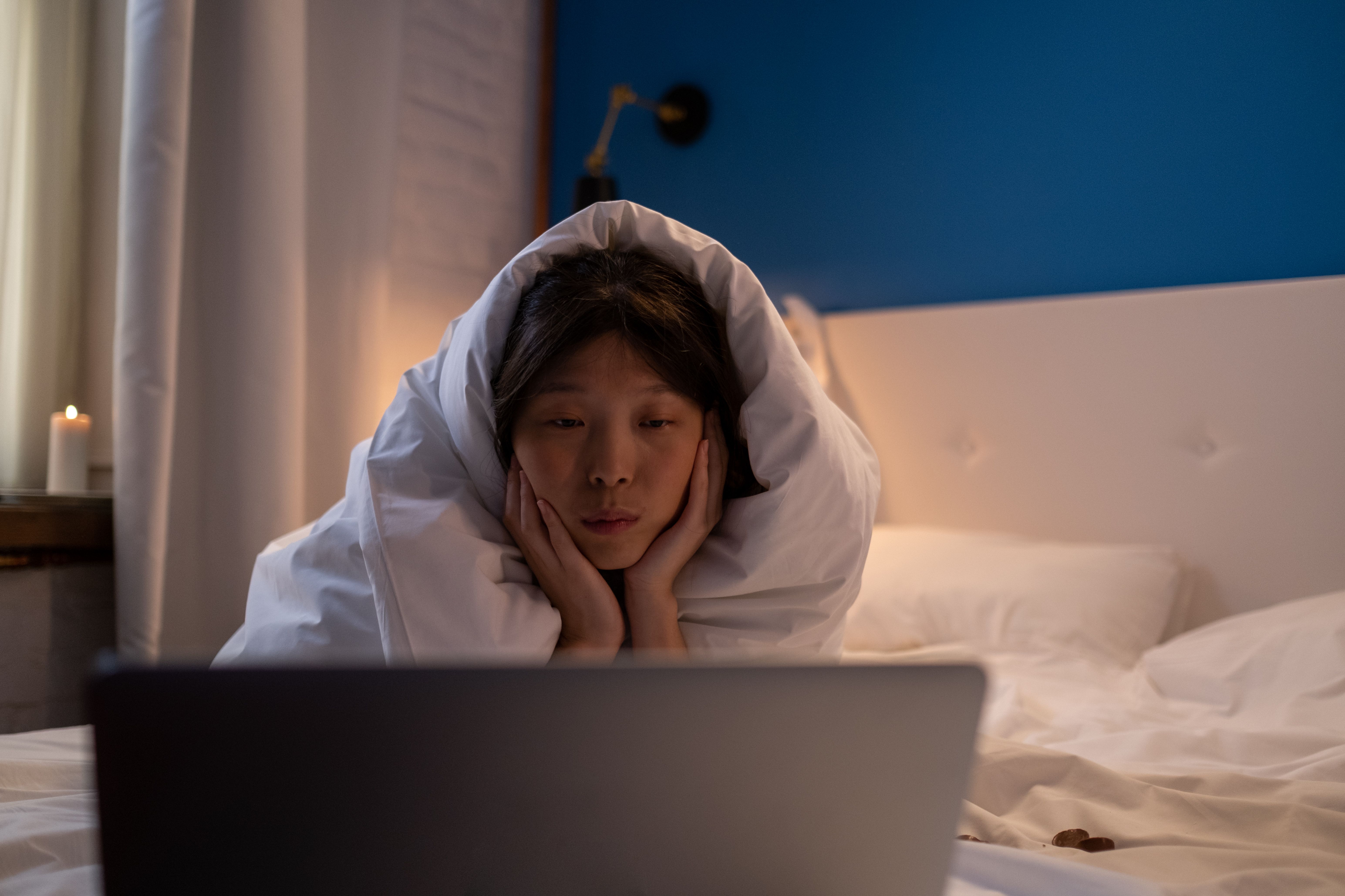 A person wrapped up in sheets watching a laptop