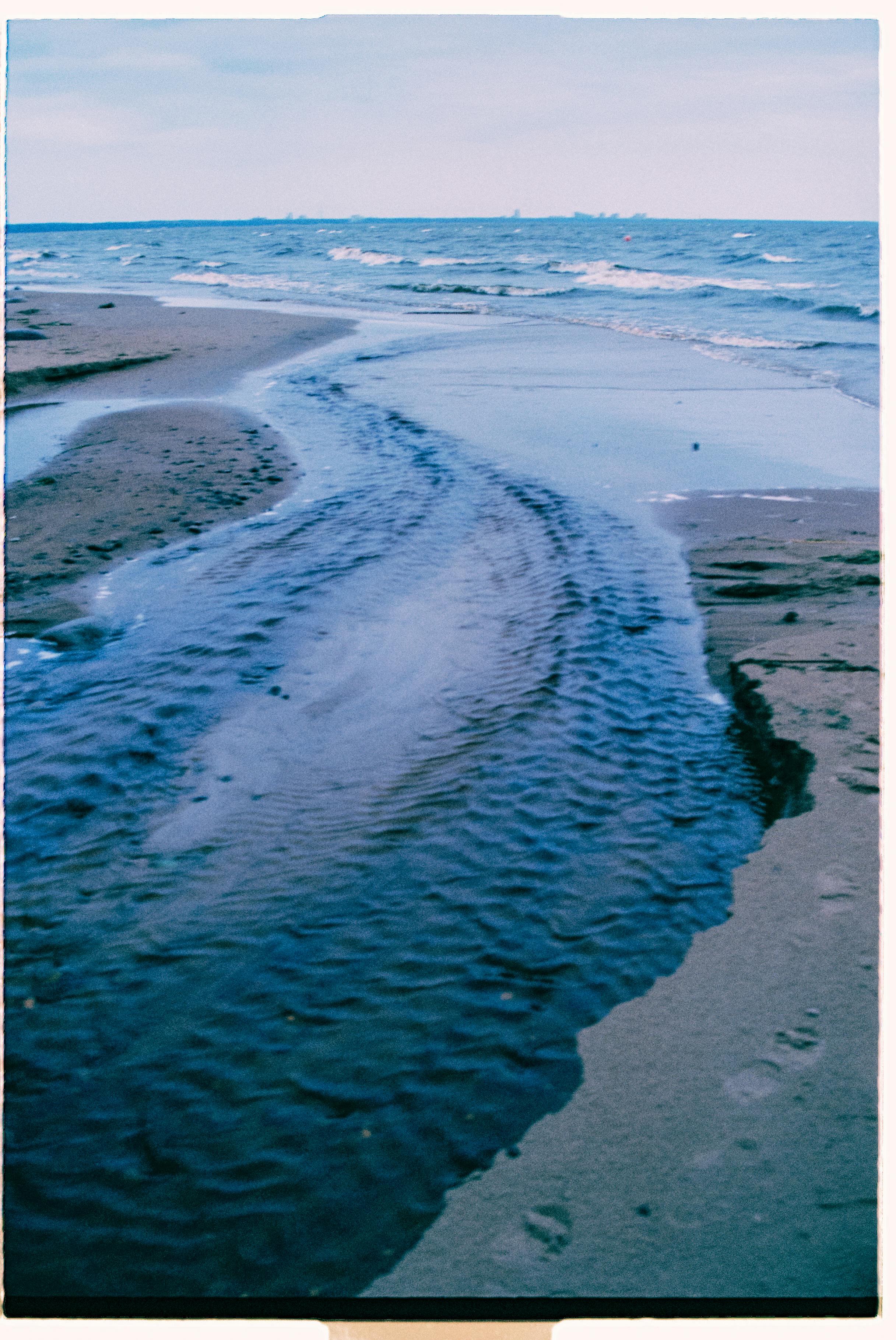 A tranquil beach scene with gentle water ripples and expansive horizon under a clear sky.