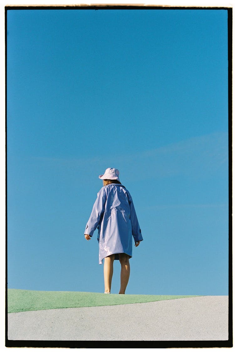 Woman In Blue Coat And Hat Against Sky