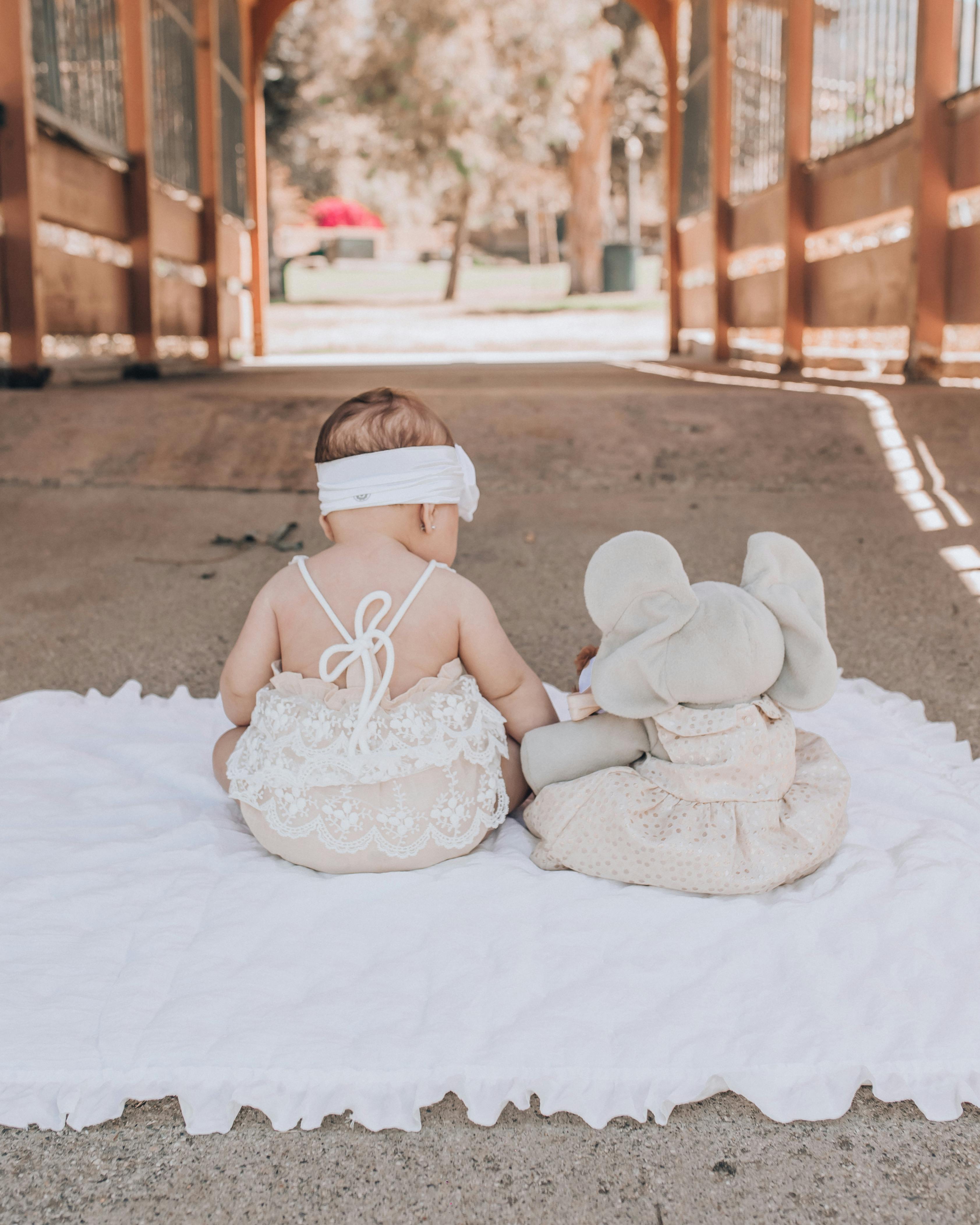Baby in White Dress Sitting on White Textile · Free Stock Photo
