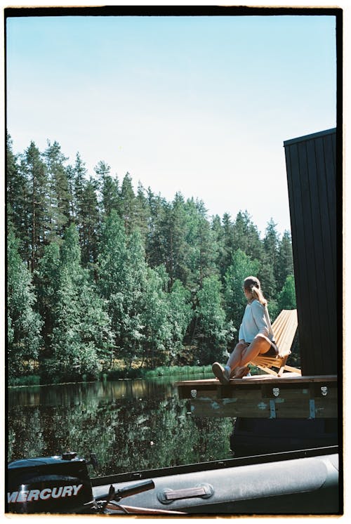 Woman in Gray Sweater Sitting on Wooden Chair near Body of Water