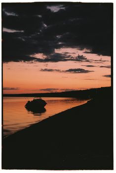 A tranquil scene of a boat silhouetted against a vibrant sunset by the sea shore.
