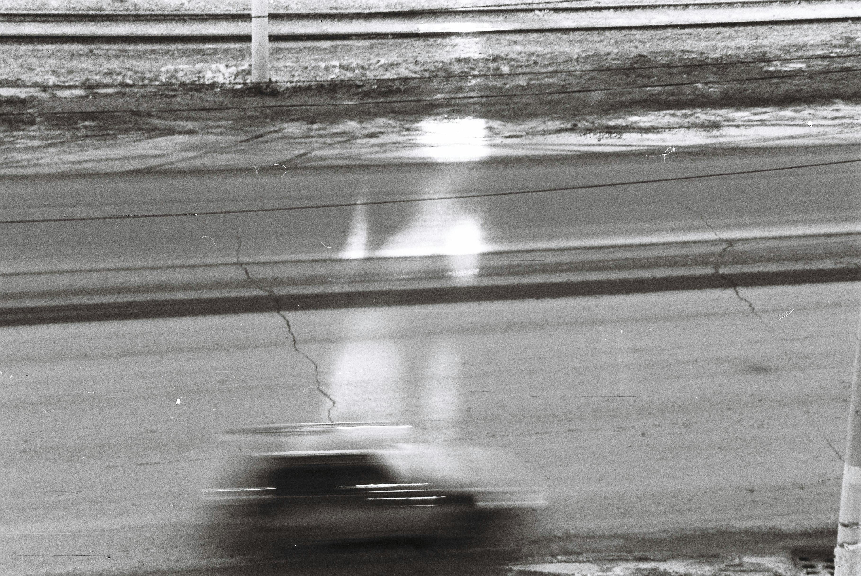 A black and white photo capturing the motion blur of a speeding vehicle on a cracked road.