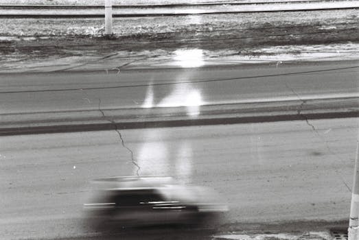 A black and white photo capturing the motion blur of a speeding vehicle on a cracked road.